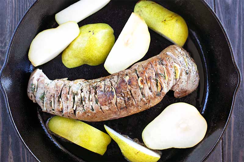 Browned meat and cut pears in a large black cast iron pan.