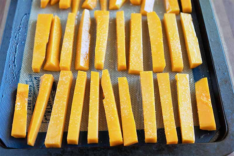 Thick nearly uniform sticks of raw butternut squash arranged in three rows on a baking sheet.