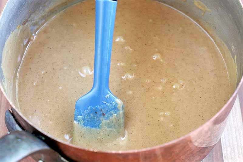 A wooden spatula stirs a peanut butter caramel mixture in a copper pot.