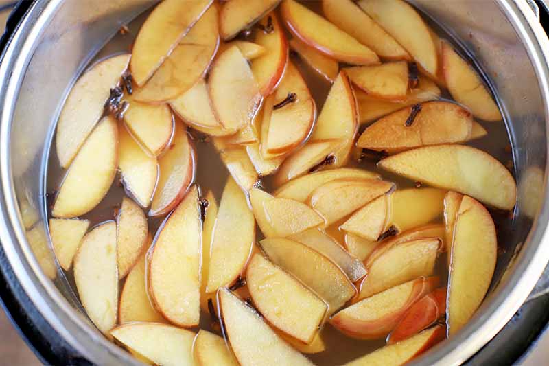 Top-down shot of sliced apples floating in liquid in a crock pot, with whole cloves.