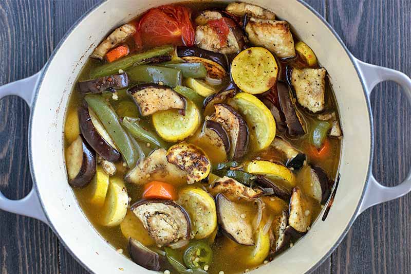 Roasted vegetables and brown broth in a white and blue enameled stockpot.