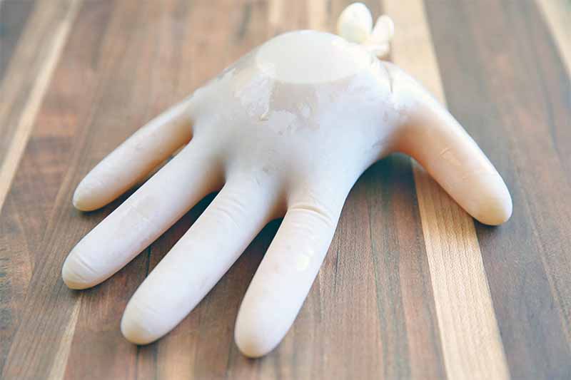 A white disposable glove is filled with liquid and tied off at the wrist, on a striped wooden surface.