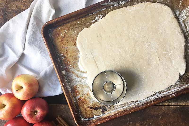 Horizontal image of cutting rolled dough on a baking sheet.