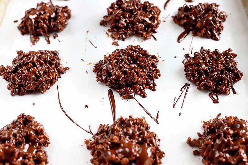 Crisped rice and sunflower seed clusters coated with chocolate, arranged in three rows on a white parchment paper background.