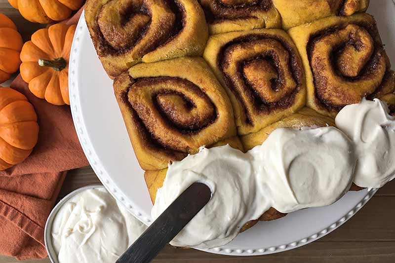 Horizontal image of icing cinnamon rolls with a spatula.