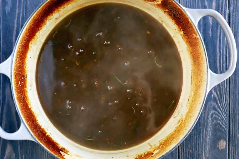Top-down shot of a pot of brown boiling and steaming broth, on a dark brown wood surface.
