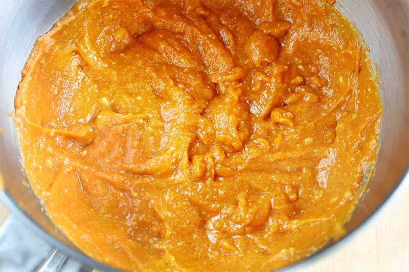 Orange pumpkin puree mixed with other ingredients in a stainless steel mixer bowl.