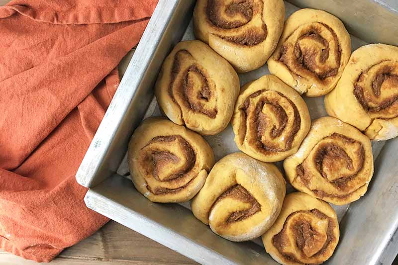 Horizontal image of a pan of unbaked cinnamon buns in a metal pan.