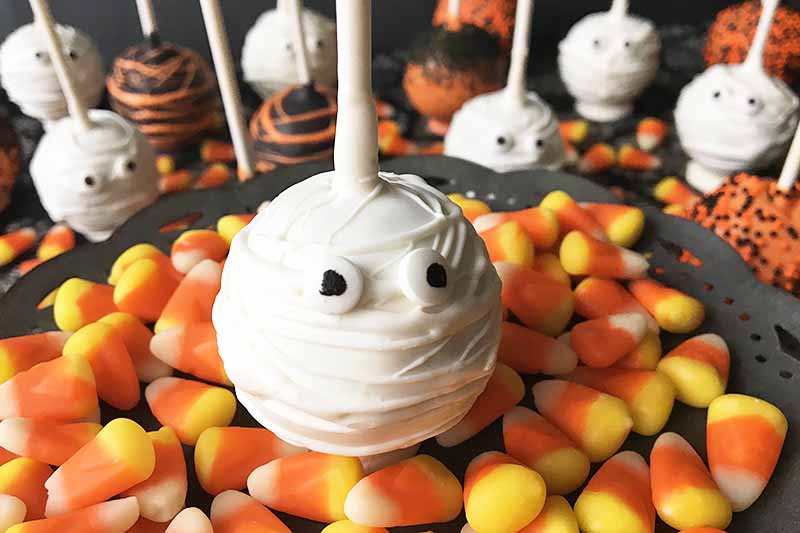 Horizontal image of assorted Halloween-themed desserts on sticks with candy corn.