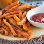 Baked butternut squash fries piled on a white plate with a small white bowl of ketchup.