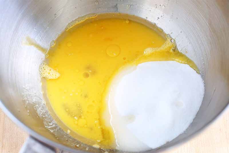 Beaten egg and a pile of white granulated sugar, in the bottom of a stainless steel stand mixer bowl.