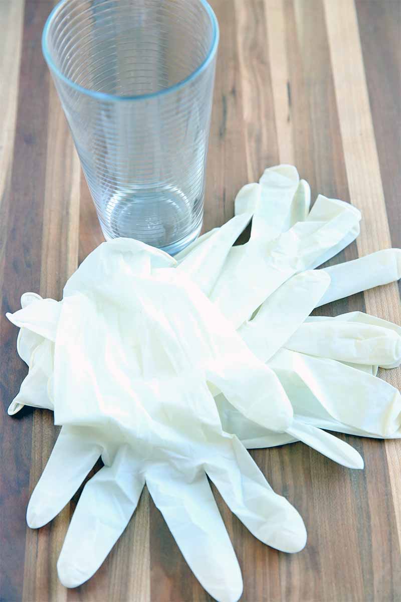 A pile of white disposable gloves and a tall drinking glass, on a wooden surface.