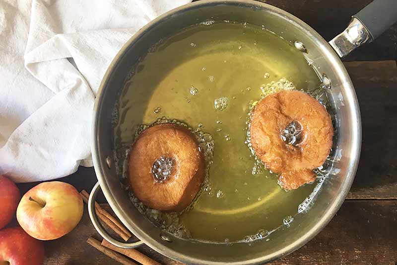 Horizontal image of deep-frying two doughnuts in a large pan.