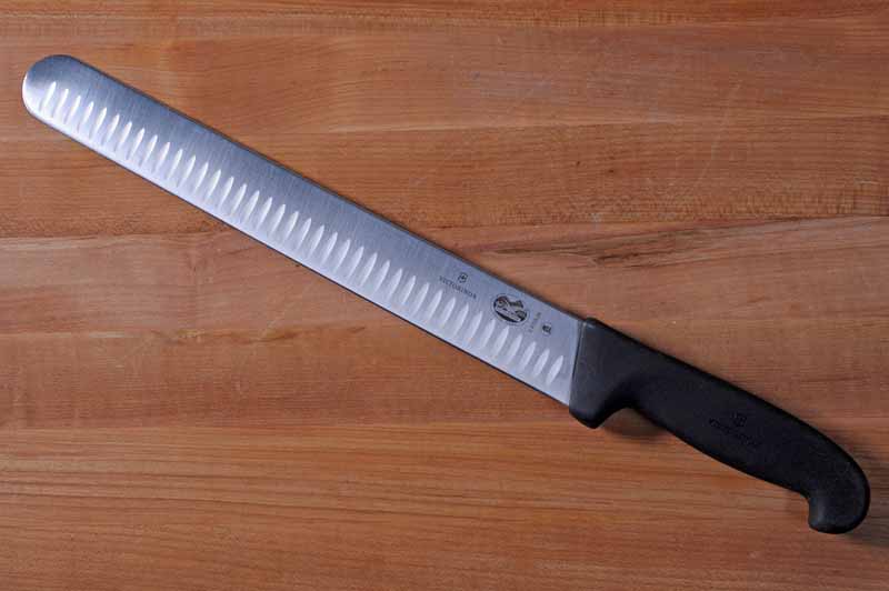 Victorinox 12 Inch Fibrox Pro Slicing Knife with Granton Blade on a maple wooden table. Top down view.