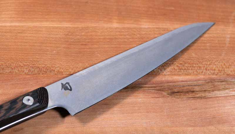 Close up of the blade of the Shun Kanso Utility Knife. The blade is on a maple wooden tabletop.