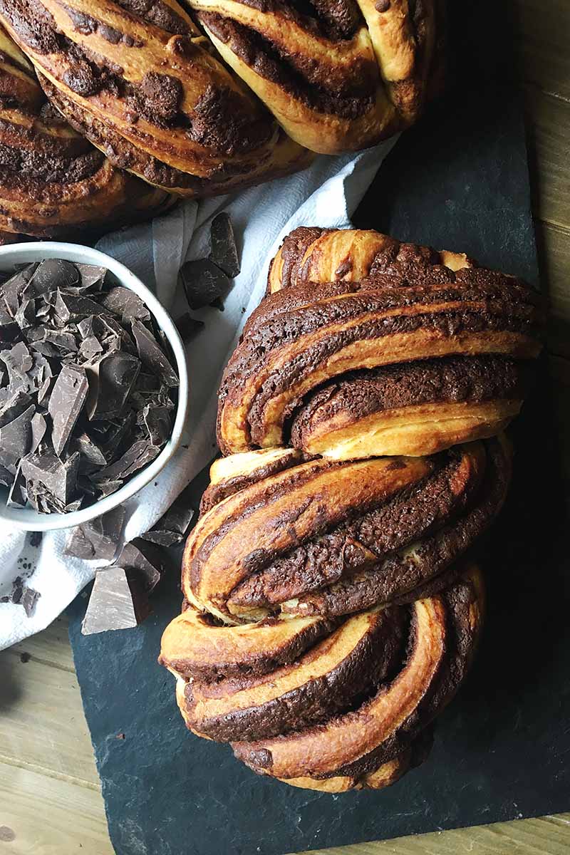 Vertical image of two whole loaves of pastry next to a bowl of dark candy.