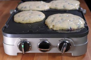 A close up of the Cuisinart GR-4N 5-in-1 Griddler showing the front dials and blueberry pancakes cooking on top.