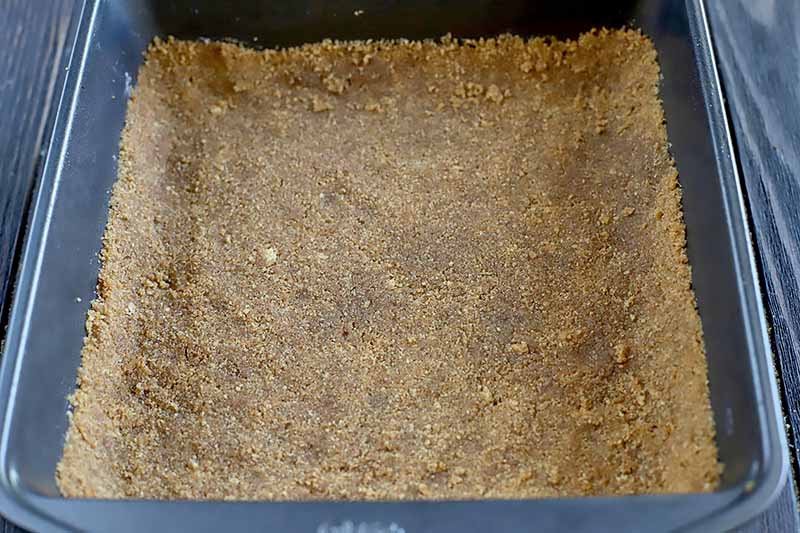 Horizontal image of a graham cracker crust pressed in a square pan.