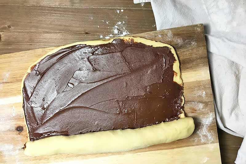 Horizontal image of a dough halfway rolled up with chocolate filling.