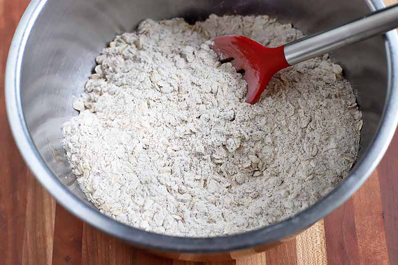 Horizontal image of a spatula stirring oats and other dry ingredients in a bowl.
