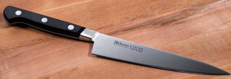 The Misono UX10 5.9 Inch Petty Knife with the blade slanted downwards and to the right on a maple cutting board.