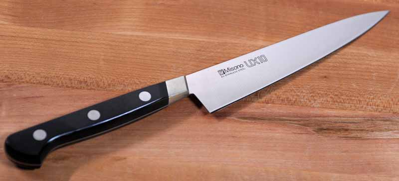 The Misono UX10 5.9 Inch Petty Knife with the blade slanted upwards and to the right on a maple butcher block.