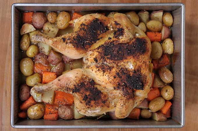 Top down view of a tasty spatchcocked and roasted lemon chicken with veggies in a rimmed baking pan and prepared in a convection toaster oven.
