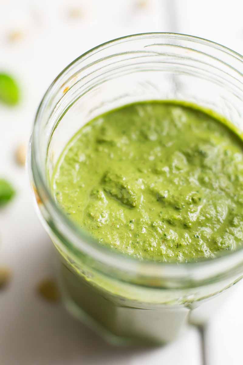 Vertical closeup image of a jar of pesto on a white surface.