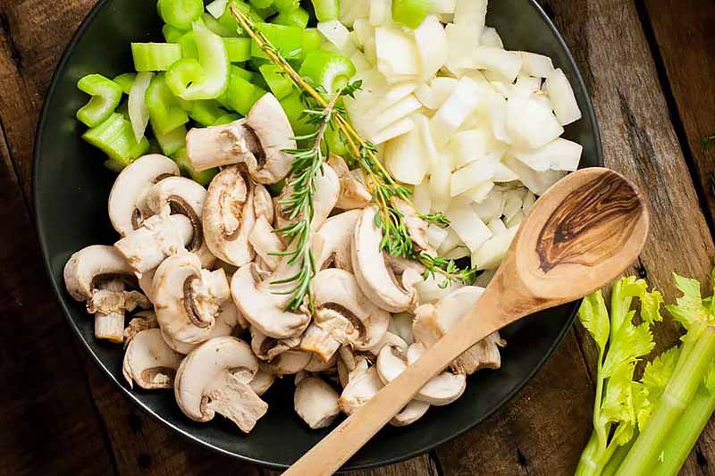 Horizontal image of assorted vegetables and a wooden spoon in a dark pan.