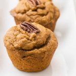 Horizontal close-up image of two pumpkin muffins with pecans on top of a white plate.