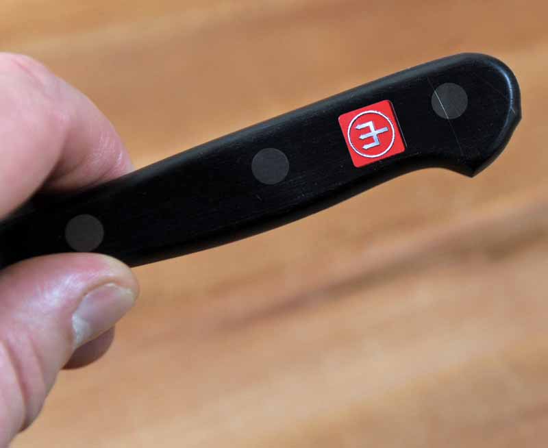 Close up of the black handle and red Wusthof symbol on the Classic 4.5 in. Asian Utility Kitchen Surfer Knife. On a wooden maple cutting board.