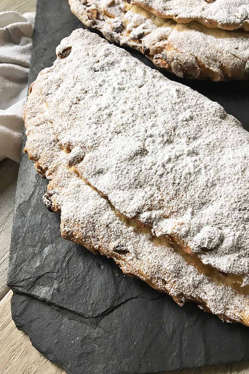 Vertical image of a whole loaf of bread generously dusted with powdered sugar on a slate board.
