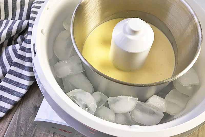 Horizontal image of ice cream base in an ice cream maker surrounded by ice cubes.