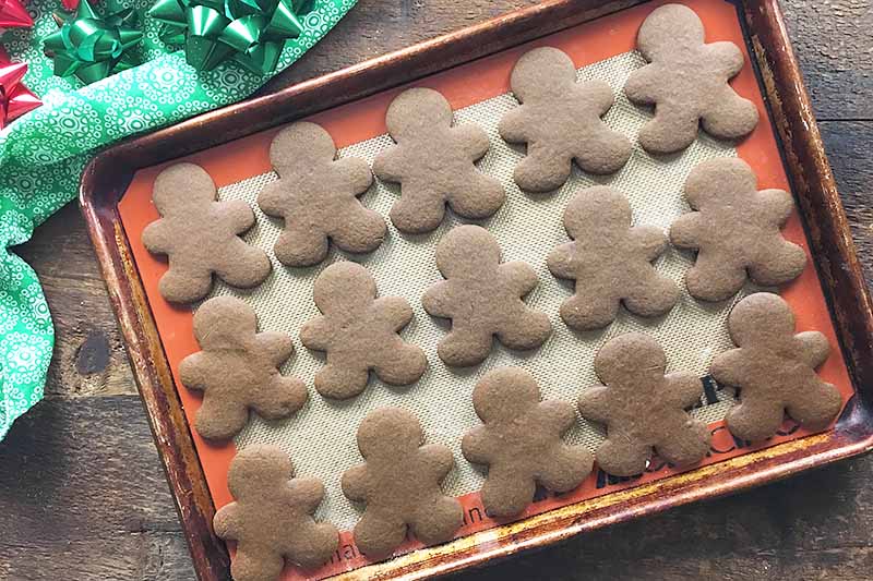 Horizontal image of a tray of baked gingerbread men cookies on a wooden surface next to a green towel.