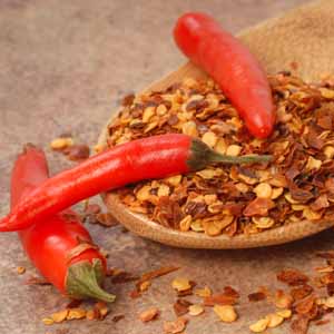 A wooden spoon full of dried chili flakes with three fresh red peppers.