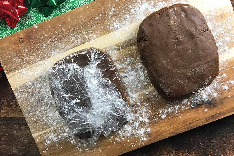 Horizontal image of two rectangles of brown dough on a floured surface, with one dough wrapped in cellophane.