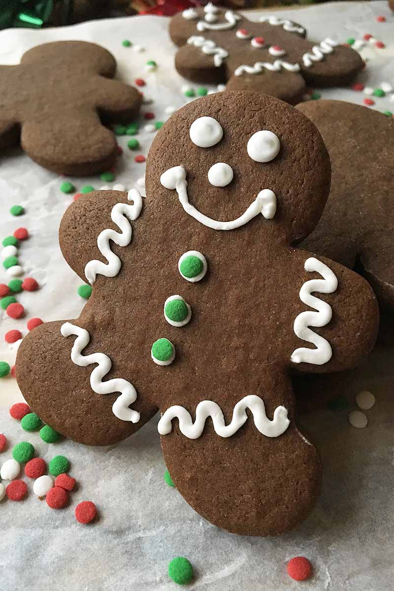 Vertical close-up image of a gingerbread men on parchment paper with sprinkles.