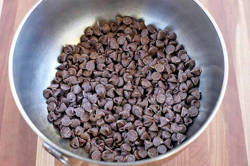 A stainless steel mixing bowl of chocolate chips on a wood countertop.