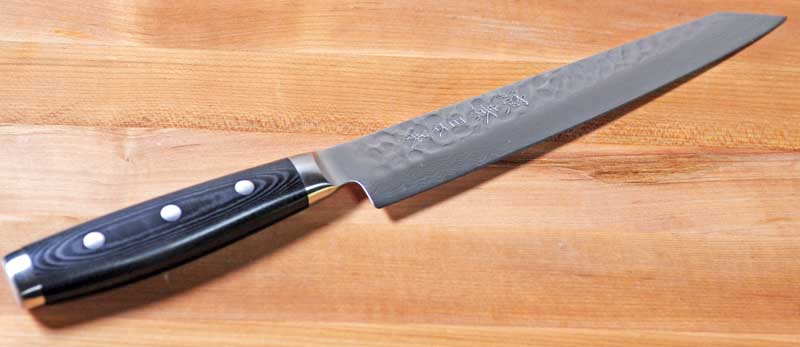 Slightly oblique view of the Enso HD Hammered Damascus 9-inch Slicing Knife on a maple butcher block surface.