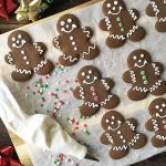 Horizontal image of decorated Christmas cookies on a work surface lined with parchment paper.