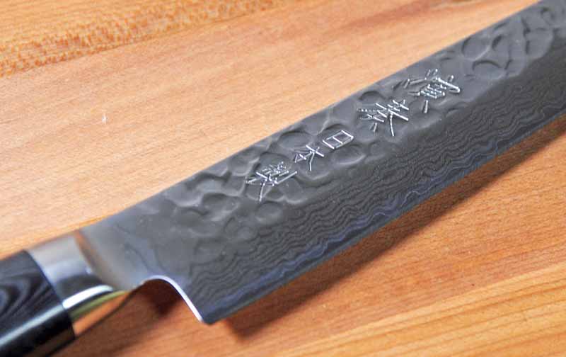A closeup of the blade on the Enso HD Hammered Damascus 9-inch Slicing Knife showing a combination of the hammering and Damascus patterning along with the engraved kanji script.