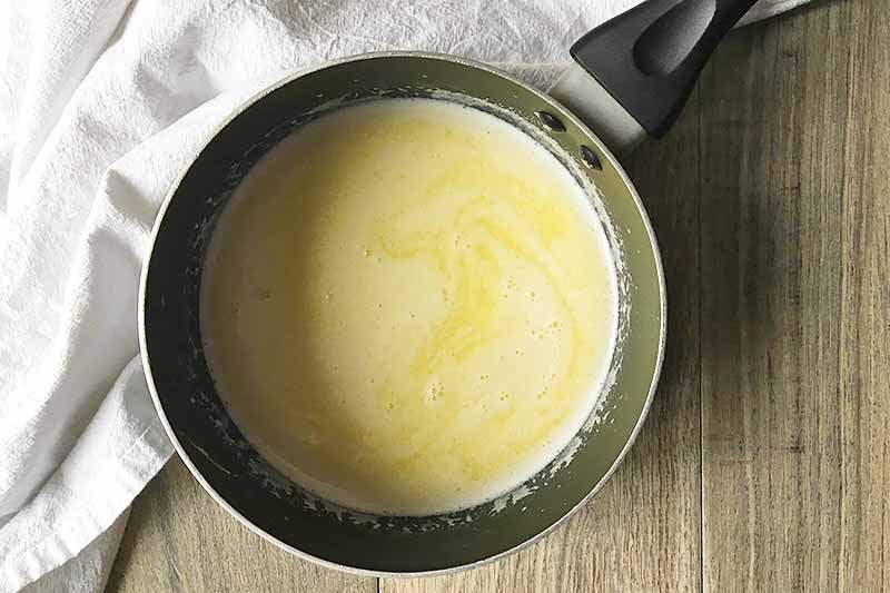 Horizontal image of a melted butter and liquid mixture in a small saucepan.