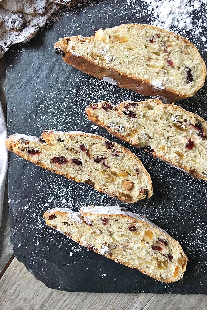 Vertical image of thin slices of stollen on a slate dusted lightly with flour.