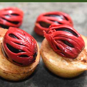 A close up of red fresh mace wrapping around nutmeg sees.