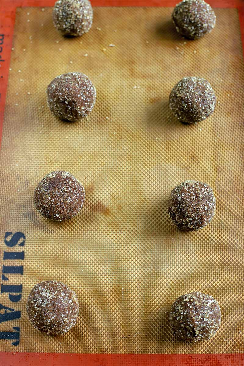 Small balls of chocolate cookie dough rolle in sugar are arranged on a Silpat silicone nonstick baking liner.