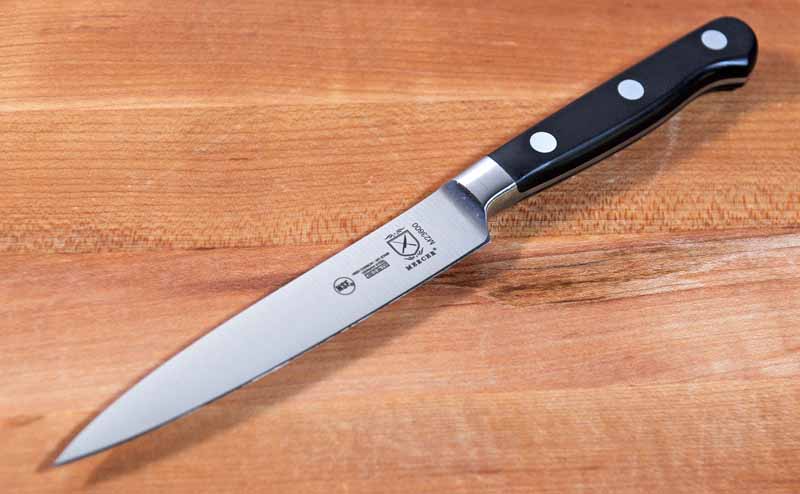 The Mercer Culinary Renaissance 5-Inch Forged Utility Knife sitting on a maple wood butcher block surface.