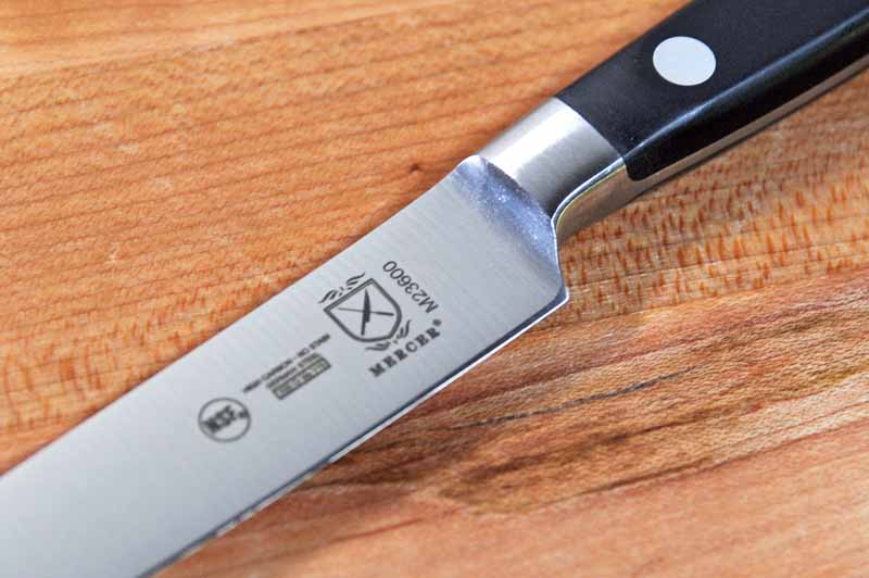A close up of the blade and laser etched logo on the Mercer Culinary Renaissance 5-Inch Forged Utility.
