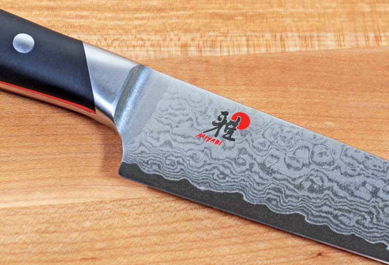 Details of the laser-etched logo and the Damascus cladding on the Miyabi Fusion Morimito Edition 9-Inch Slicing Knife.