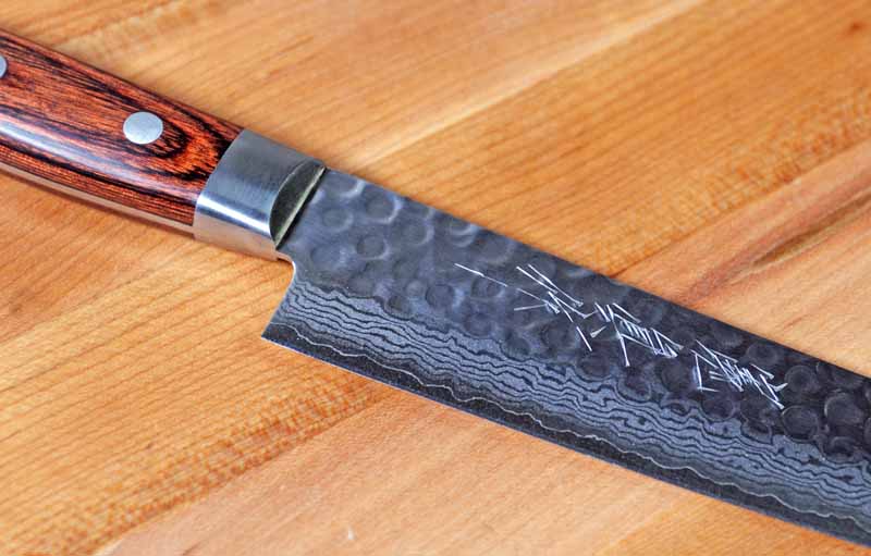 A closeup of the handle, bolster, hammered and Damascus finish, as well as the engraved kanji script on the Norisada.