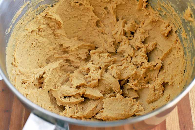 Beaten peanut butter dough in a stainless steel mixing bowl on a wood surface.